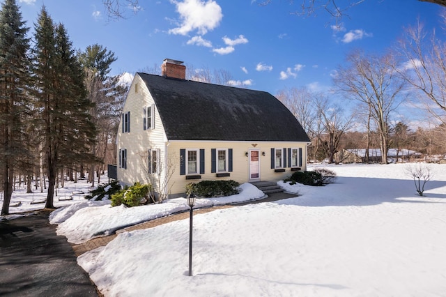 dutch colonial featuring roof with shingles and a chimney