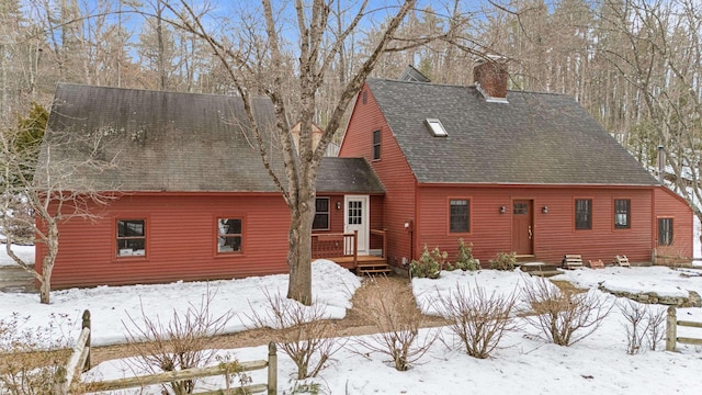 snow covered rear of property featuring a chimney, a wooden deck, and a shingled roof