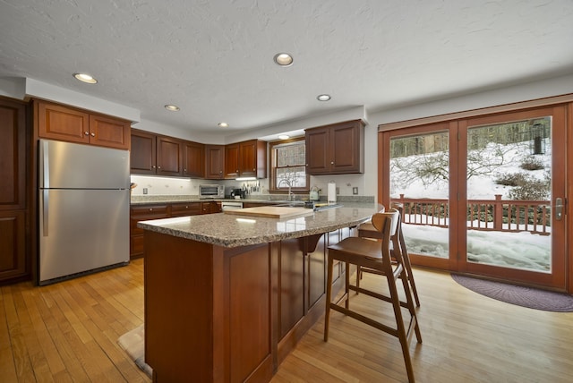 kitchen with a textured ceiling, recessed lighting, light wood-style floors, appliances with stainless steel finishes, and a breakfast bar area