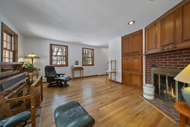 sitting room with light wood-style flooring, a baseboard heating unit, a textured ceiling, baseboards, and a brick fireplace