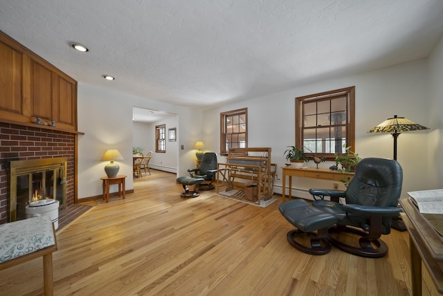 interior space with light wood-type flooring, baseboard heating, a brick fireplace, and a textured ceiling