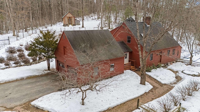 snow covered property with a garage, driveway, roof with shingles, and a chimney