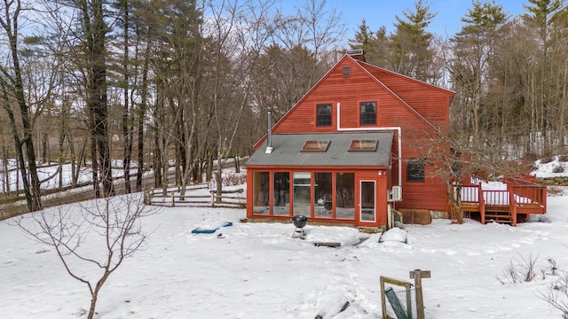 snow covered back of property with fence, a wooden deck, roof with shingles, a chimney, and a sunroom