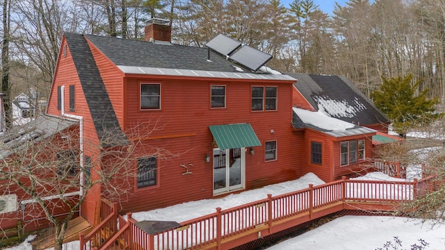 snow covered back of property featuring a wooden deck, roof with shingles, and a chimney