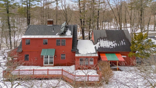 snow covered rear of property featuring roof with shingles and a chimney