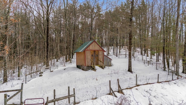 snow covered structure featuring an outdoor structure, fence, and a view of trees