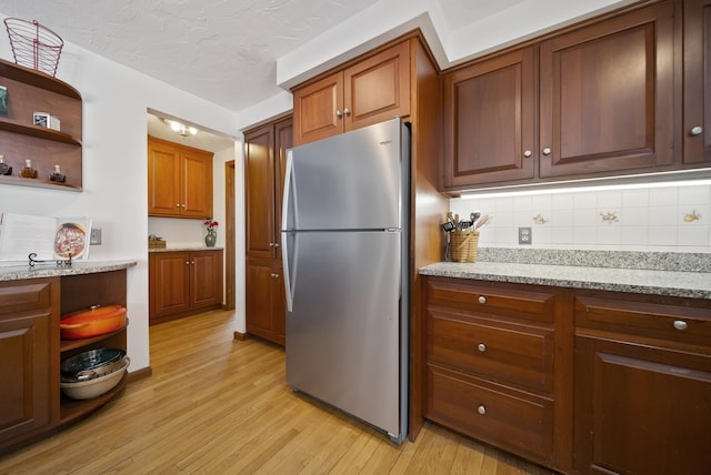 kitchen with open shelves, light stone counters, light wood-style floors, and freestanding refrigerator