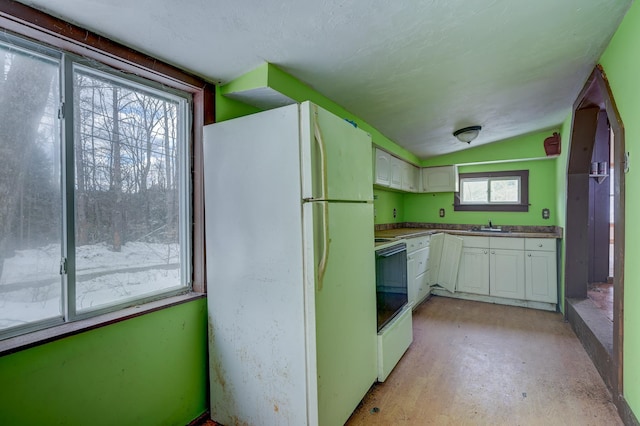 kitchen featuring concrete floors, lofted ceiling, white cabinets, white appliances, and a sink