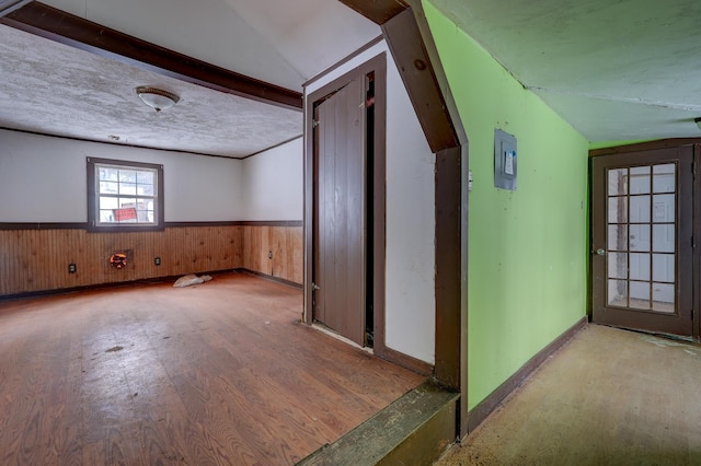 interior space with wooden walls, wood finished floors, wainscoting, vaulted ceiling, and a textured ceiling