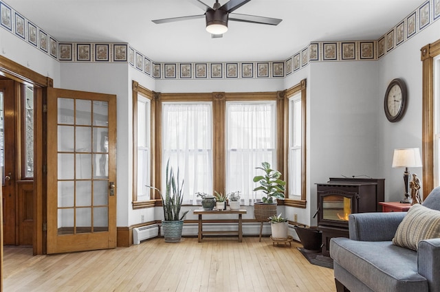 sitting room featuring baseboard heating, a wood stove, ceiling fan, and hardwood / wood-style flooring