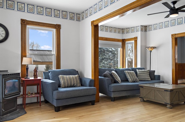 living area featuring light wood-type flooring, a wood stove, and a ceiling fan