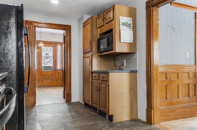 kitchen with dark countertops, backsplash, a wainscoted wall, brown cabinetry, and black appliances