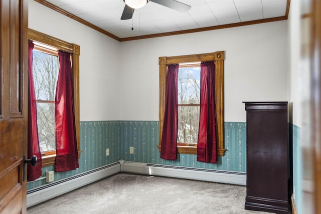 carpeted spare room featuring a baseboard heating unit, ornamental molding, a ceiling fan, and wallpapered walls