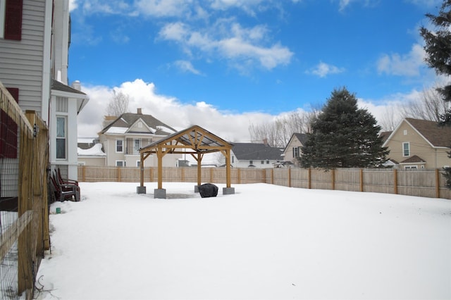 snowy yard with a gazebo, a fenced backyard, and a residential view