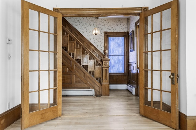 foyer featuring wood finished floors, french doors, wallpapered walls, a baseboard radiator, and stairs