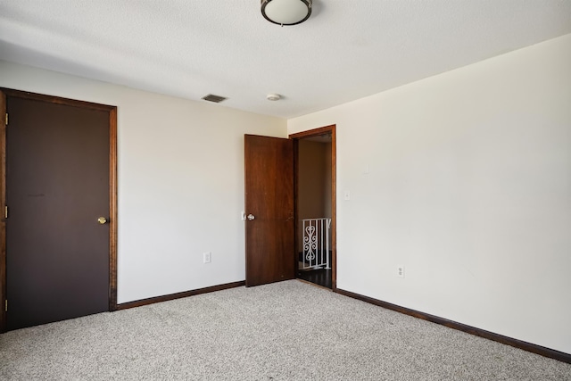 carpeted spare room with visible vents, a textured ceiling, and baseboards