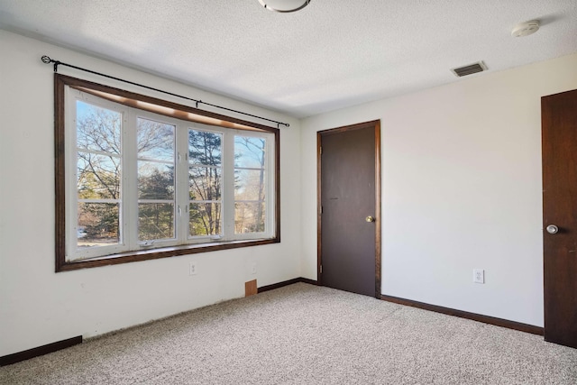 carpeted spare room featuring visible vents, baseboards, and a textured ceiling