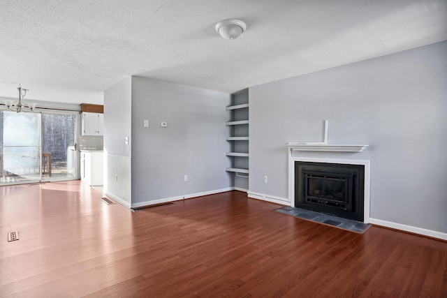 unfurnished living room with built in features, wood finished floors, baseboards, a fireplace with flush hearth, and a textured ceiling