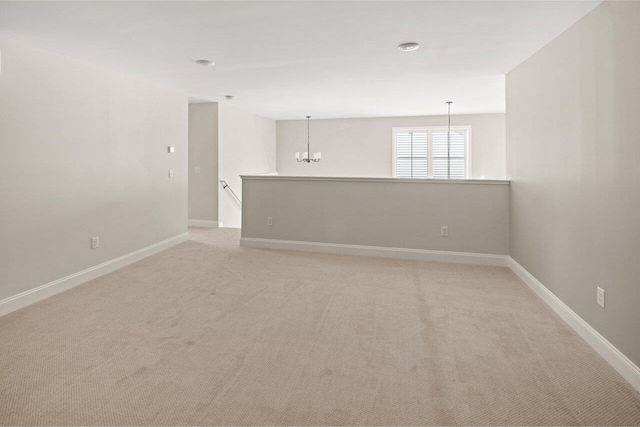 empty room with baseboards, light carpet, and a chandelier