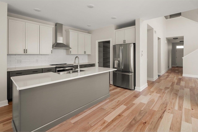 kitchen featuring a sink, appliances with stainless steel finishes, wall chimney exhaust hood, and light wood finished floors