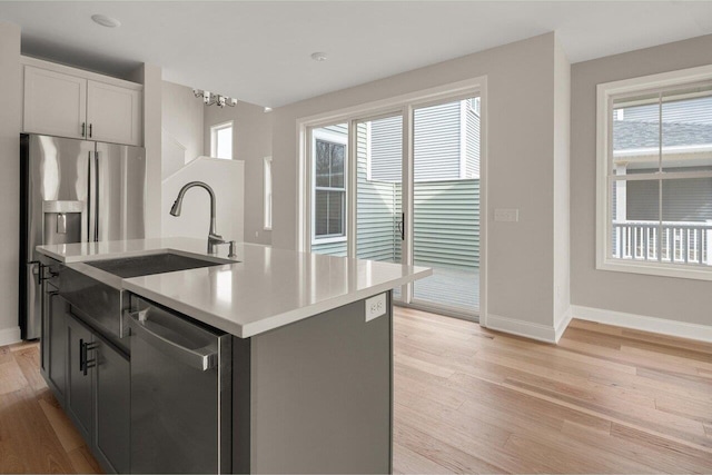 kitchen with baseboards, light wood-style flooring, a sink, stainless steel appliances, and light countertops