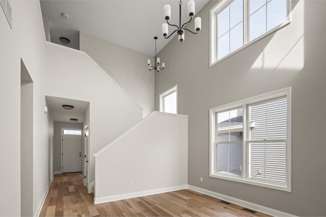 interior space with wood finished floors, baseboards, visible vents, an inviting chandelier, and a towering ceiling