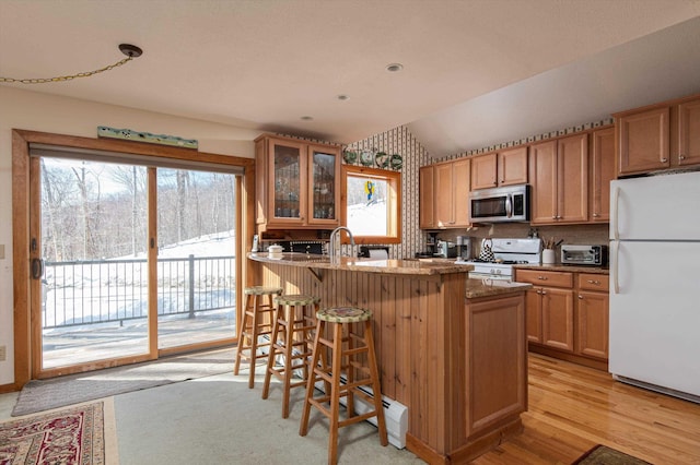 kitchen featuring a breakfast bar, white appliances, light wood-style floors, glass insert cabinets, and vaulted ceiling