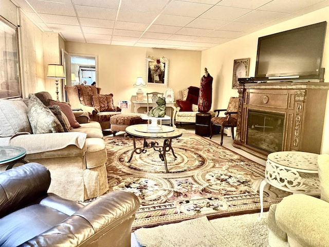 living area featuring a drop ceiling and a glass covered fireplace