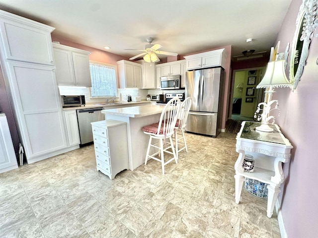 kitchen with a kitchen island, stainless steel appliances, light countertops, white cabinetry, and backsplash