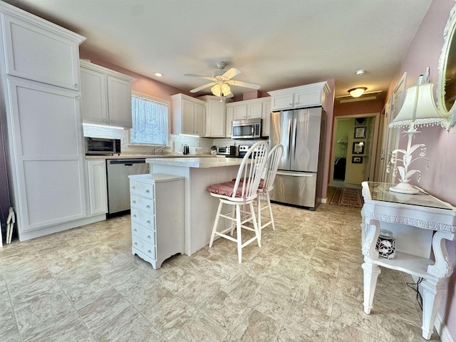 kitchen with backsplash, a kitchen island, stainless steel appliances, white cabinets, and light countertops