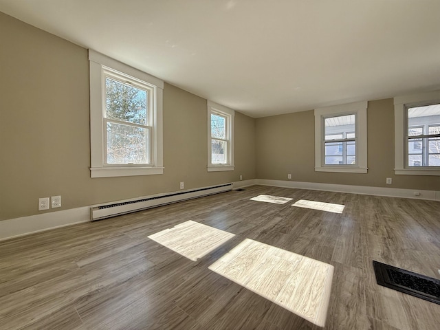 unfurnished room featuring a wealth of natural light, baseboards, baseboard heating, and wood finished floors