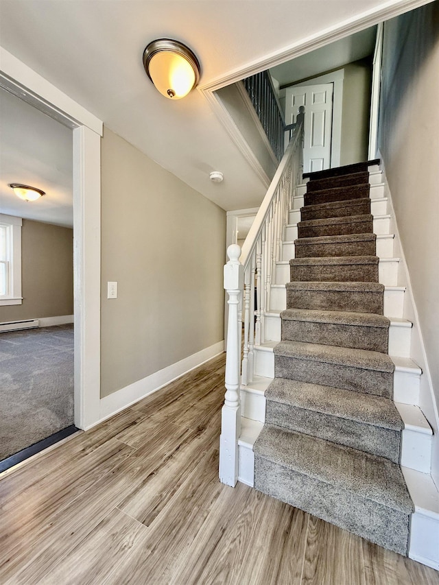 stairway with a baseboard heating unit, wood finished floors, and baseboards