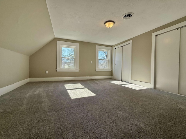 unfurnished bedroom featuring carpet, visible vents, vaulted ceiling, a textured ceiling, and two closets