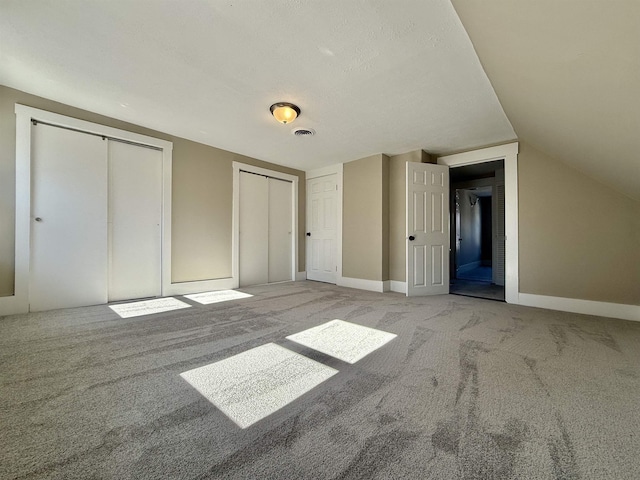 unfurnished bedroom featuring carpet, visible vents, vaulted ceiling, multiple closets, and a textured ceiling