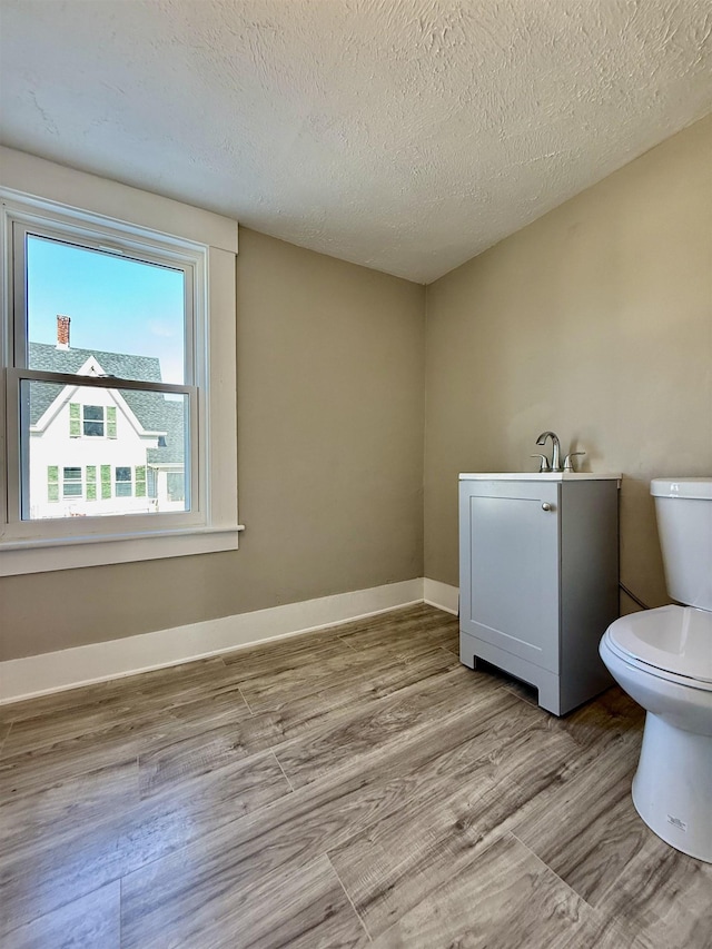 bathroom with baseboards, toilet, wood finished floors, and a textured ceiling