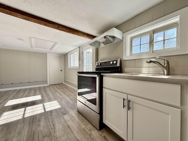 kitchen featuring under cabinet range hood, a sink, a textured ceiling, light wood-style floors, and stainless steel electric range