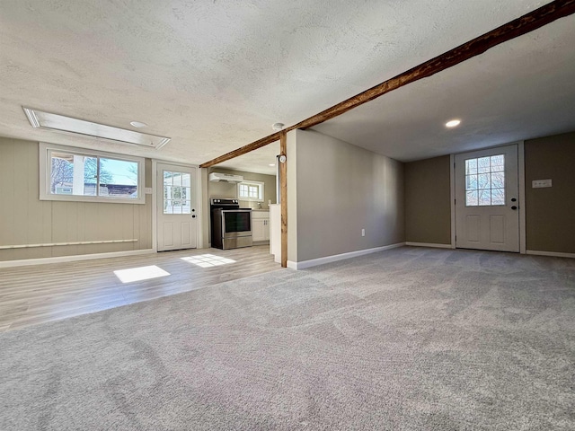 unfurnished living room with light carpet, baseboards, a textured ceiling, and a wealth of natural light