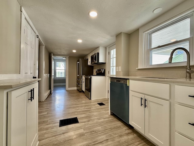 kitchen with visible vents, light wood-style flooring, stainless steel appliances, white cabinetry, and a sink