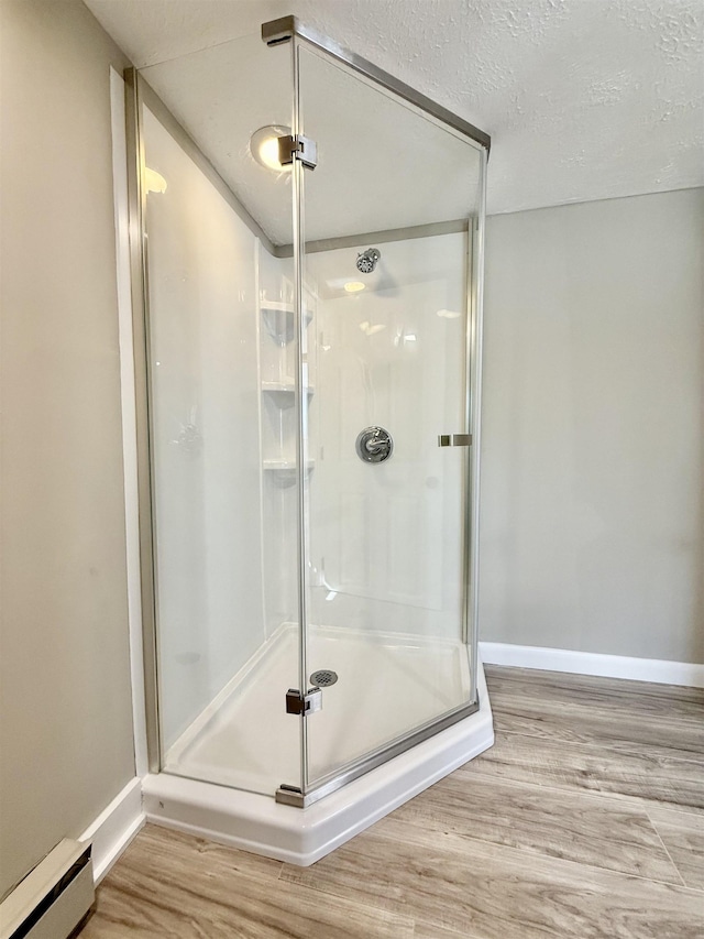 full bath featuring baseboard heating, a shower stall, baseboards, and wood finished floors