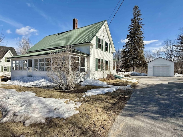 view of snowy exterior featuring aphalt driveway, a detached garage, an outdoor structure, metal roof, and a chimney