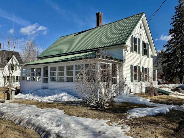 view of snow covered exterior with metal roof, a sunroom, and a chimney