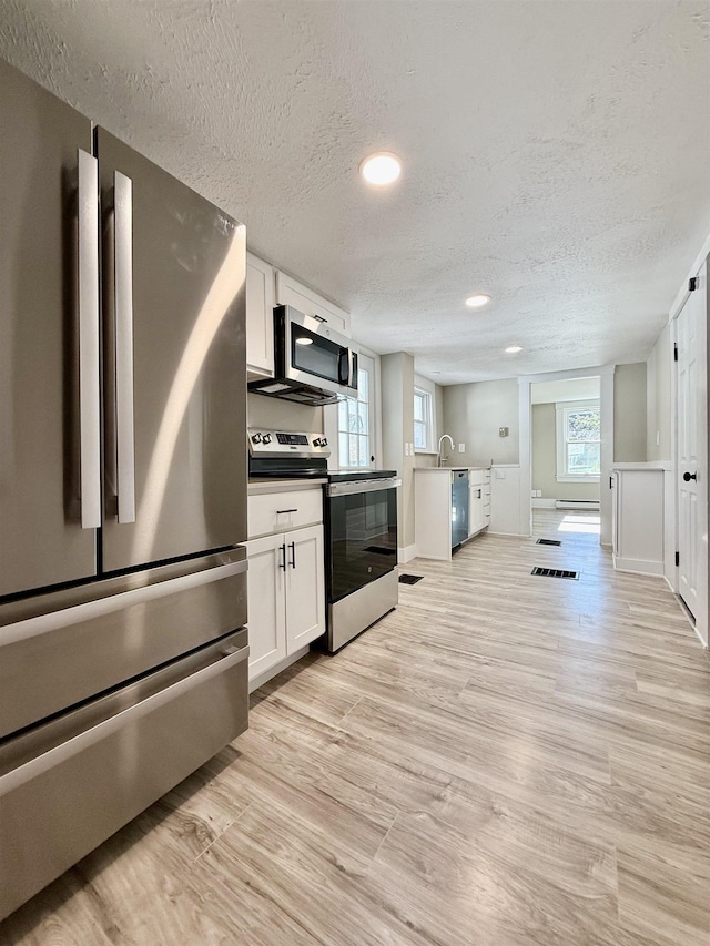 kitchen featuring light wood-style flooring, appliances with stainless steel finishes, white cabinetry, and a textured ceiling