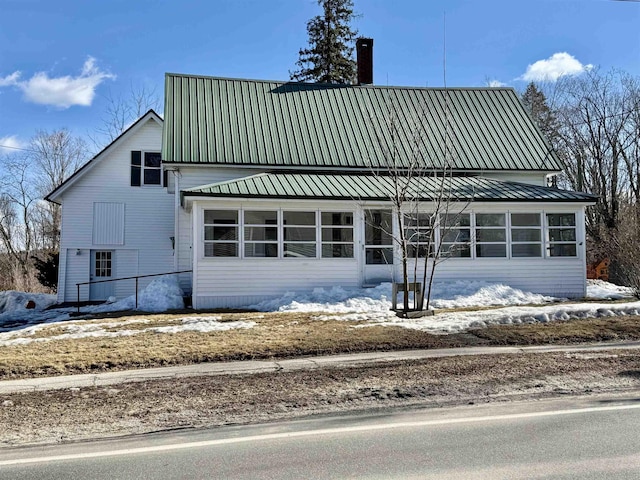 view of front of home with metal roof, a chimney, and a sunroom