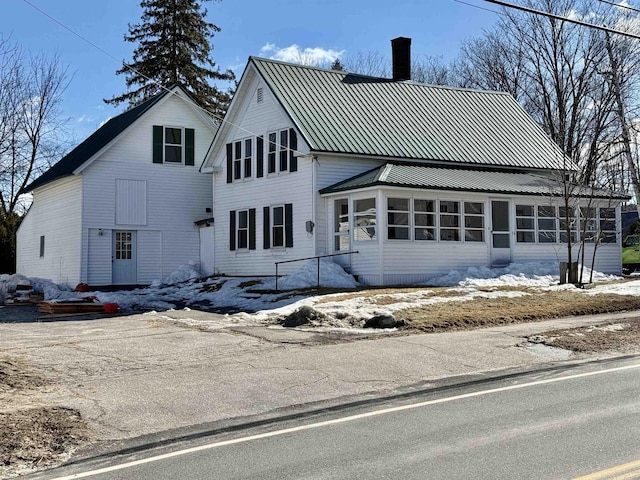 view of front of home with a standing seam roof, metal roof, a sunroom, and a chimney