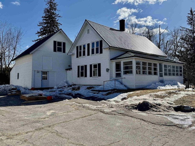 back of house featuring metal roof, a chimney, a standing seam roof, and a sunroom