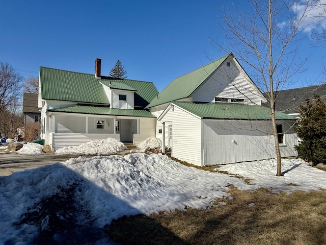 snow covered back of property with a chimney and metal roof