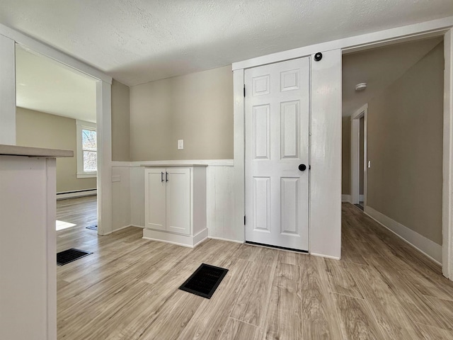 spare room featuring baseboard heating, a textured ceiling, light wood-style floors, and visible vents