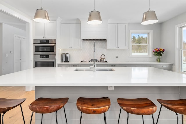 kitchen with backsplash, double oven, light countertops, white cabinets, and gas stovetop