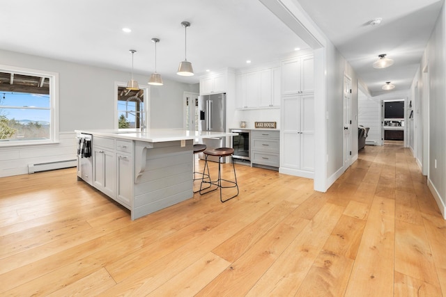 kitchen with light wood-type flooring, wine cooler, appliances with stainless steel finishes, light countertops, and a baseboard radiator