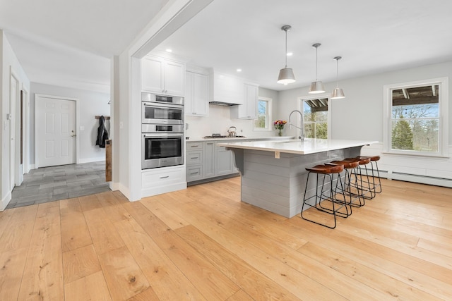 kitchen featuring tasteful backsplash, stainless steel double oven, light wood finished floors, and light countertops